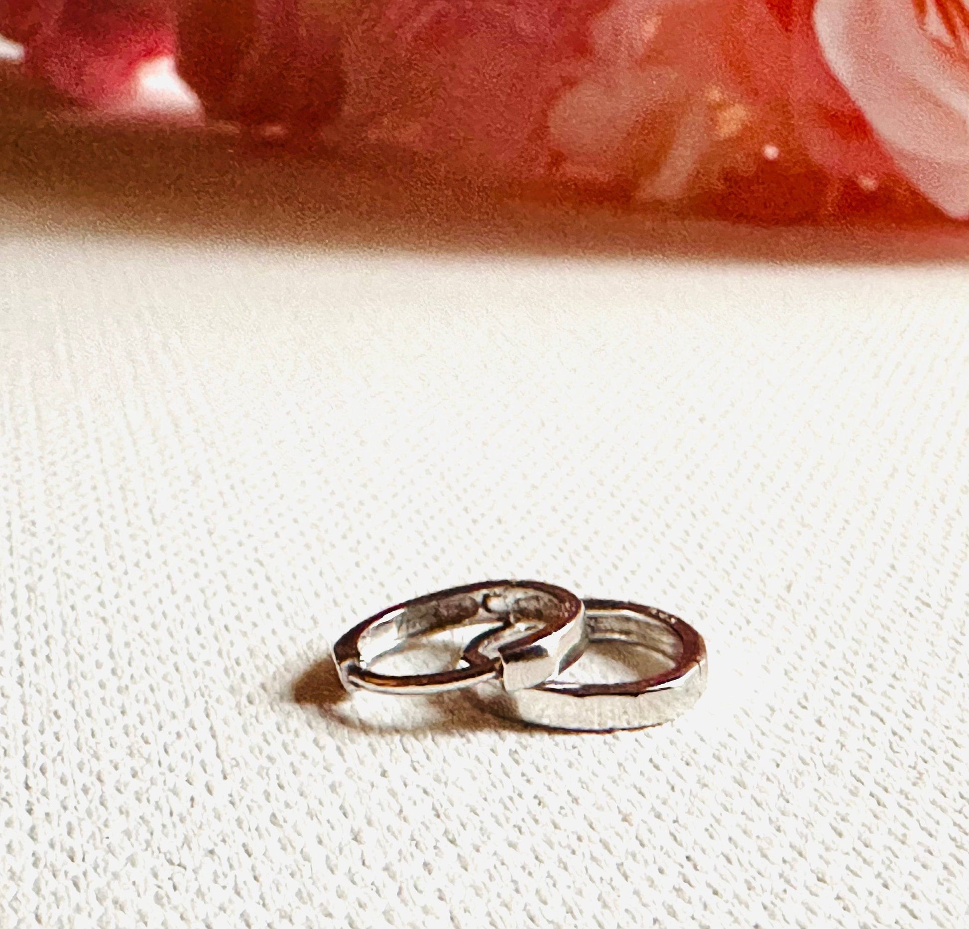 Minimalist silver huggie hoop earrings with smooth finish, placed on a light fabric. Classic hoops for versatile styling.