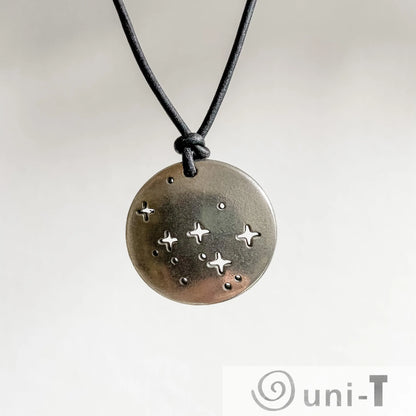 Close-up of Cassiopeia Necklace pendant with constellation star pattern, handcrafted science jewelry on adjustable black cord.