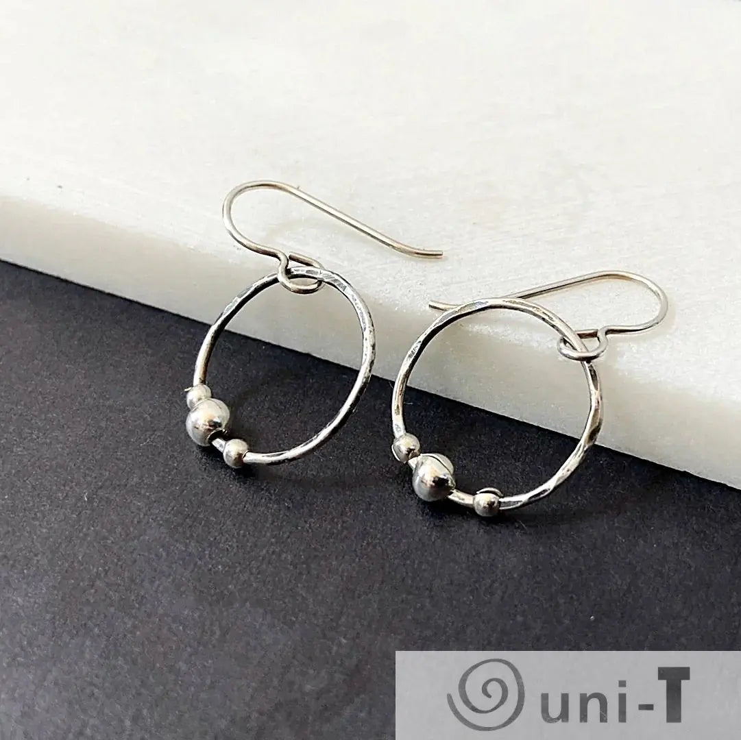 Circle Fidget Earrings from the Circle Fidget Jewelry Set, featuring hammered hoops and silver beads, displayed on a black and white surface.