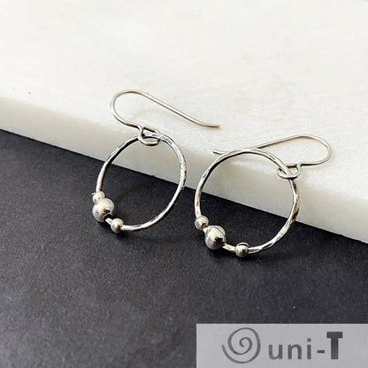 Circle Fidget Earrings from the Circle Fidget Jewelry Set, featuring hammered hoops and silver beads, displayed on a black and white surface.