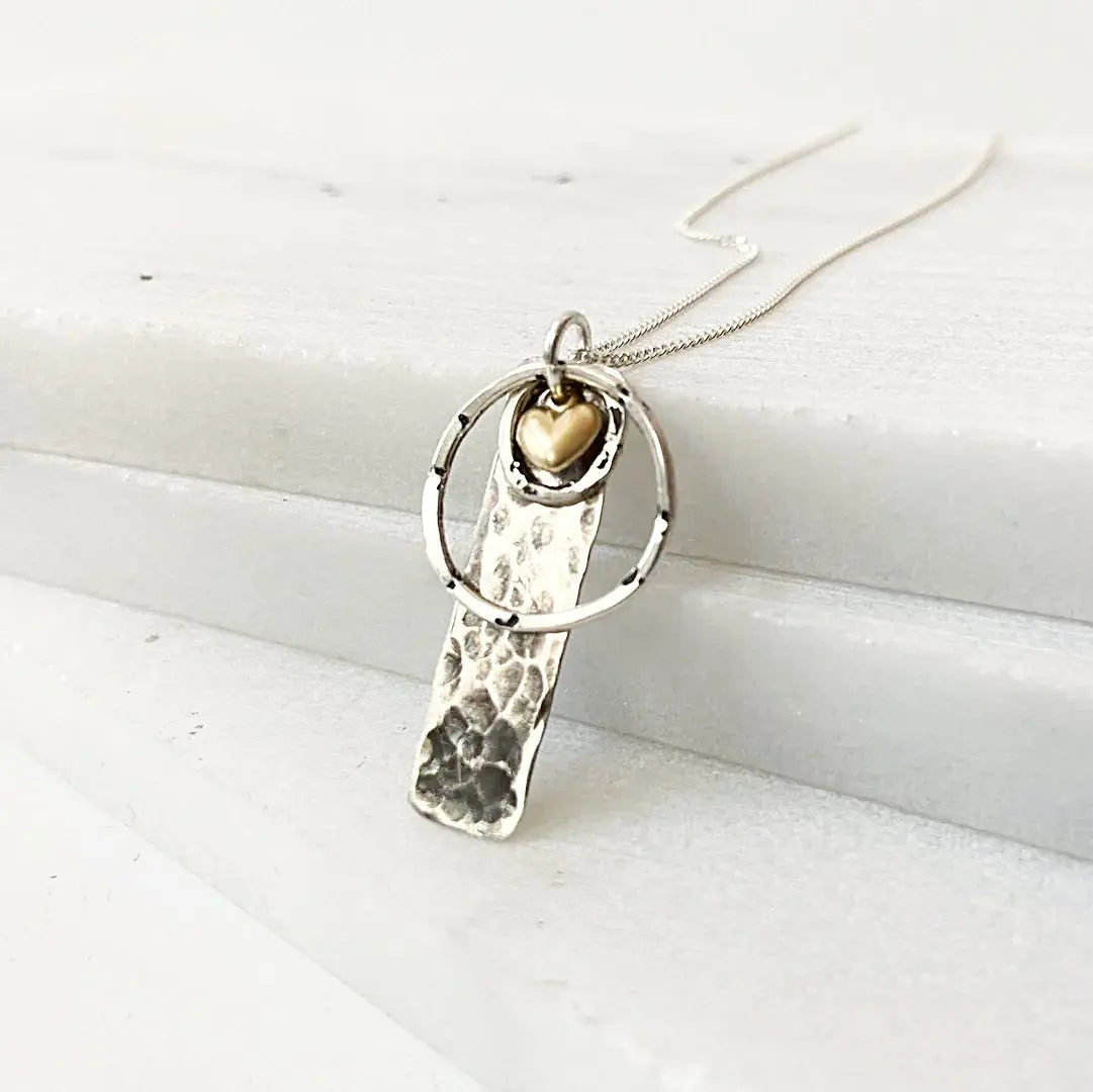 Silver Circle Tag Necklace with textured silver tag, gold heart accent, and sterling ring. Minimalist jewelry for everyday elegance.