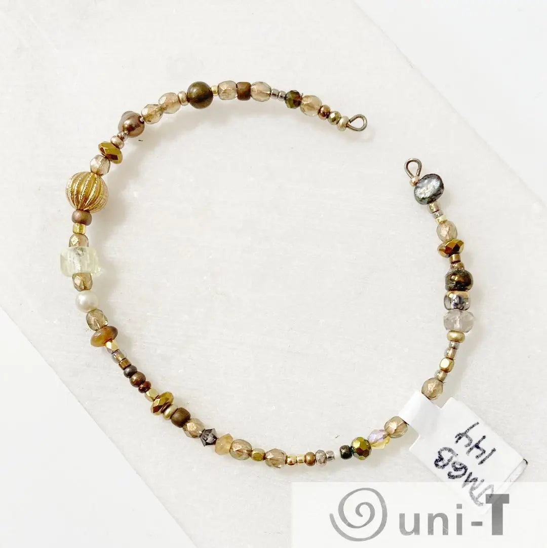 Beaded cuff bracelet with gold and bronze beads on steel wire, featuring a mix of textures and shapes. Elegant accessory for stylish outfits.