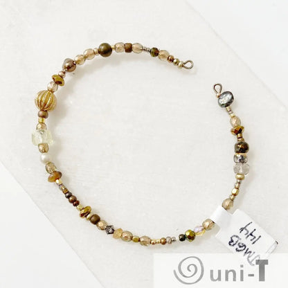 Beaded cuff bracelet with gold and bronze beads on steel wire, featuring a mix of textures and shapes. Elegant accessory for stylish outfits.