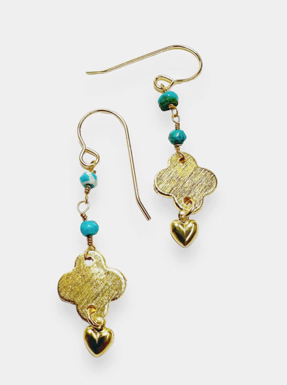 Close-up of turquoise chain earrings with gold quatrefoil and heart charms, highlighting gemstone details and brushed brass finish.
