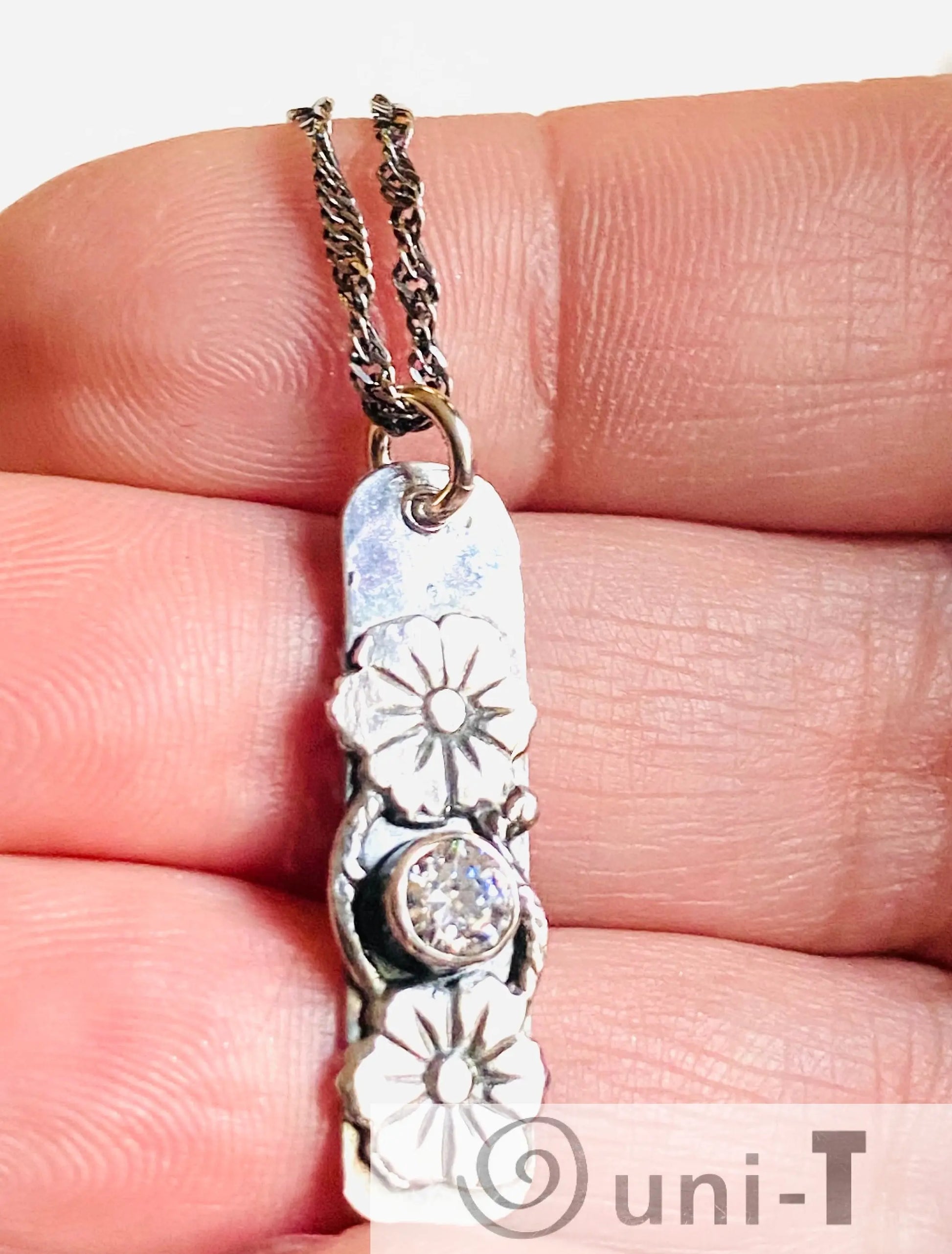 Close-up of Flower Tag Necklace pendant with cubic zirconia and floral motifs, highlighting intricate silver craftsmanship and sparkle.