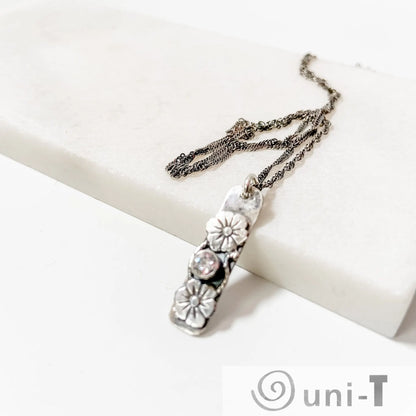 Flower Tag Necklace with cubic zirconia and floral silver tag pendant, displayed on a white marble surface with twisted rope chain.