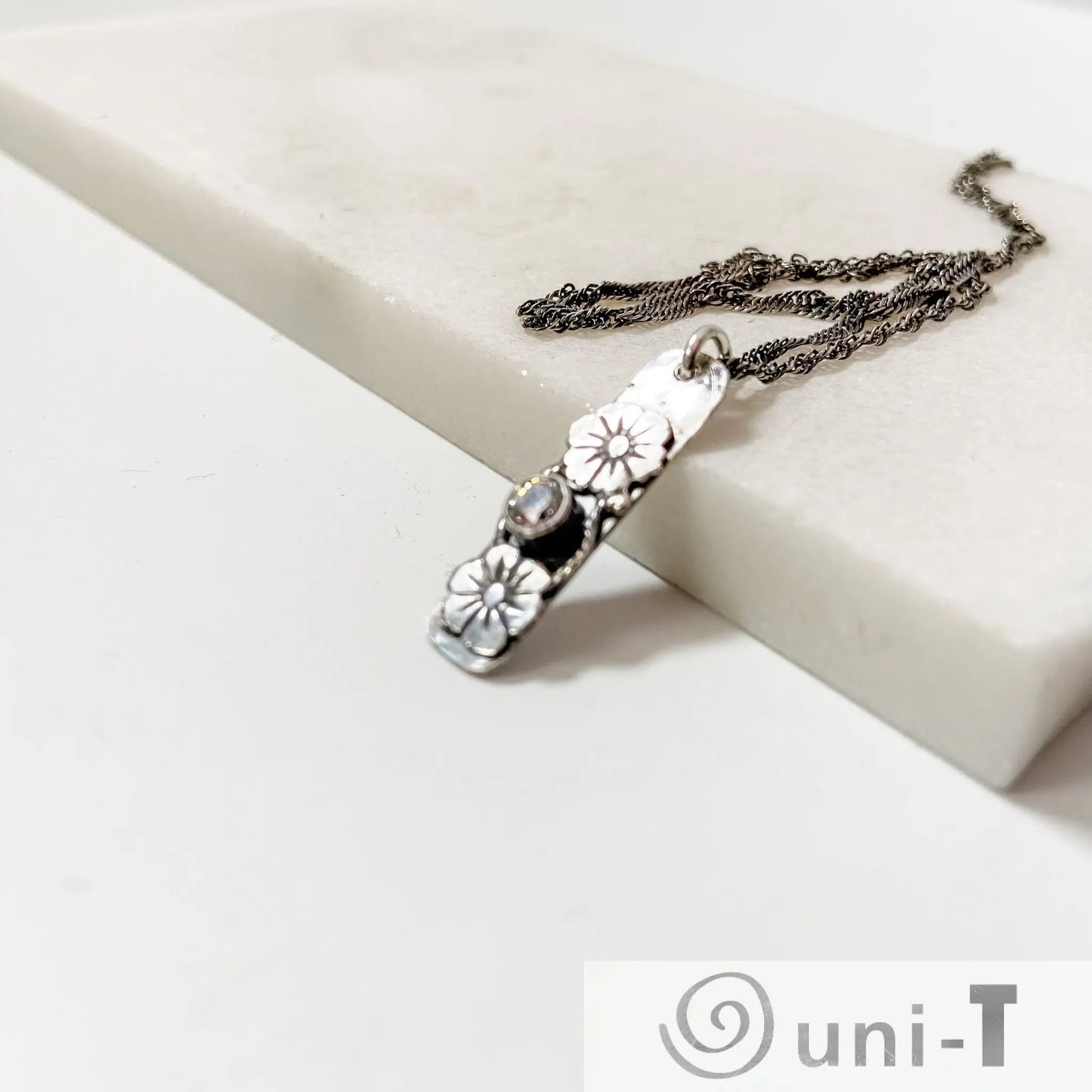 Angled view of Flower Tag Necklace featuring cubic zirconia and floral design on silver tag, paired with an antiqued sterling rope chain.