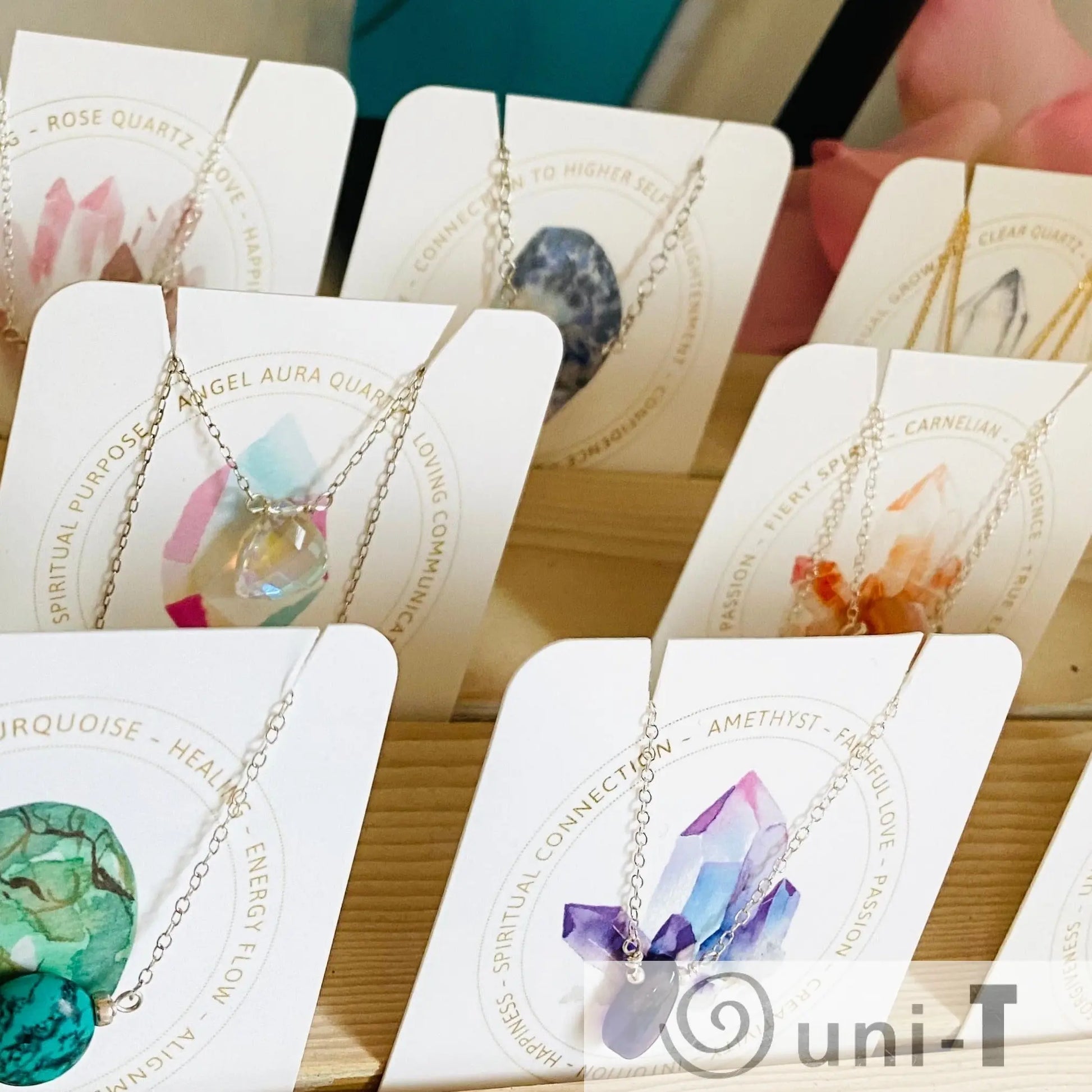 Display of gemstone necklaces with sterling silver chains and hand-cut stones, ideal as birthstone gifts. Includes amethyst, carnelian, and turquoise.