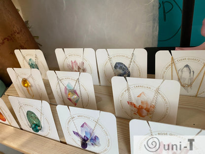 Assorted gemstone necklaces on display cards with sterling silver chains. Features birthstones like rose quartz, amethyst, and clear quartz.