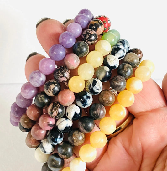 Hand holding assorted gemstone stretch bracelets featuring labradorite, agate, calcite, and chalcedony beads in various colors and patterns.