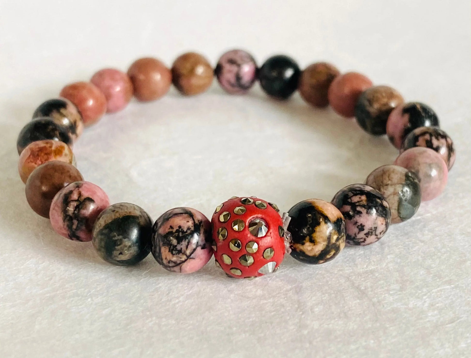 Gemstone stretch bracelet with pink and brown agate beads and a red decorative centerpiece, ideal for bold fashion statements.