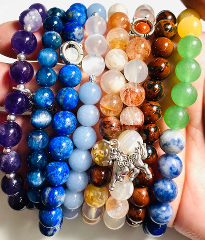 Hand holding colorful gemstone stretch bracelets including lapis lazuli, sunstone, and aventurine, ideal for gifting and stacking.