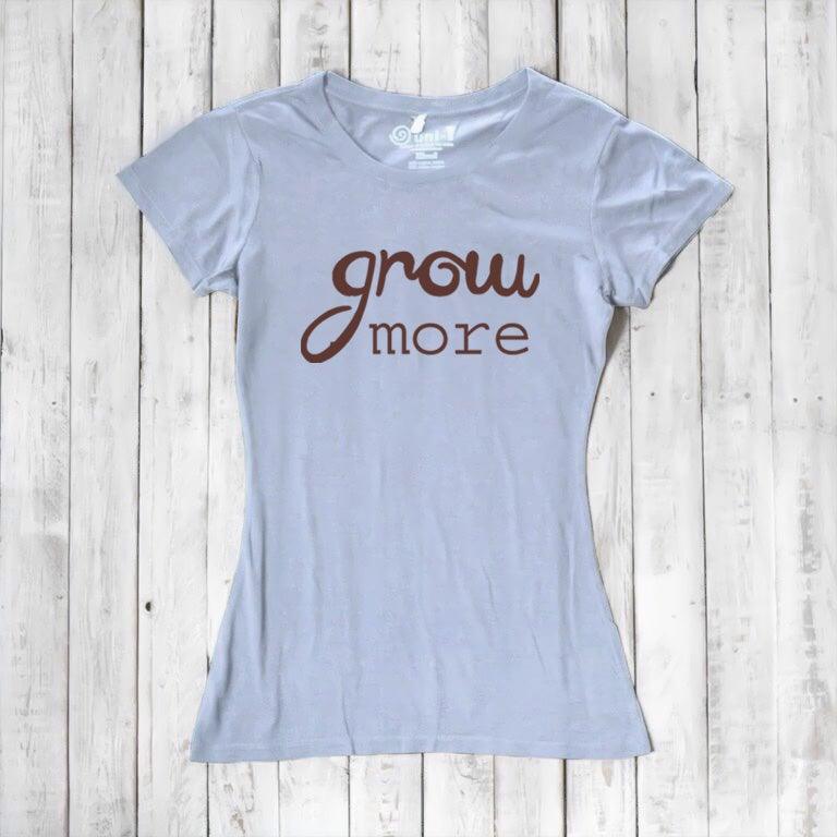 Light blue women's T-shirt with brown 'Grow More' text. Soft bamboo and organic cotton blend, ideal for plant and garden enthusiasts.