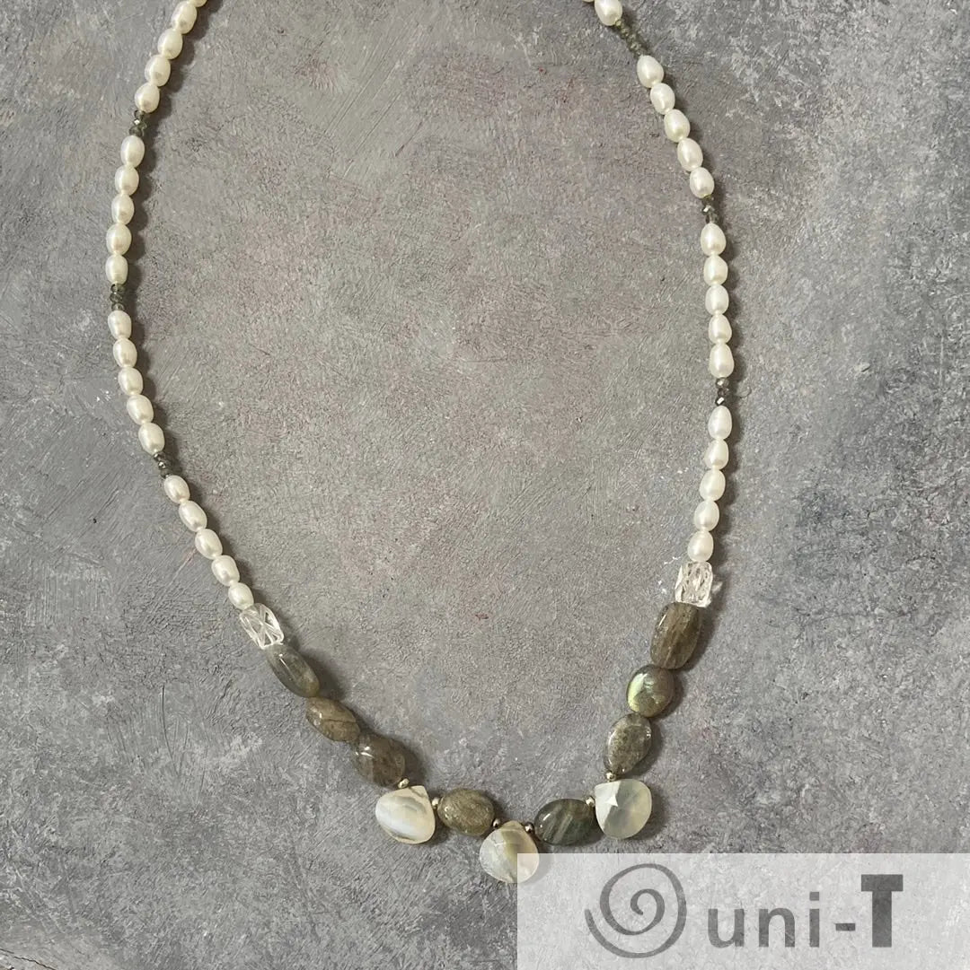 Full view of labradorite and pearl necklace with sterling silver clasp laid flat on a grey surface, highlighting gemstone textures.