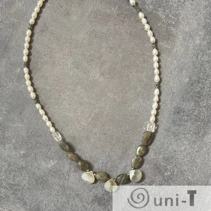 Full view of labradorite and pearl necklace with sterling silver clasp laid flat on a grey surface, highlighting gemstone textures.