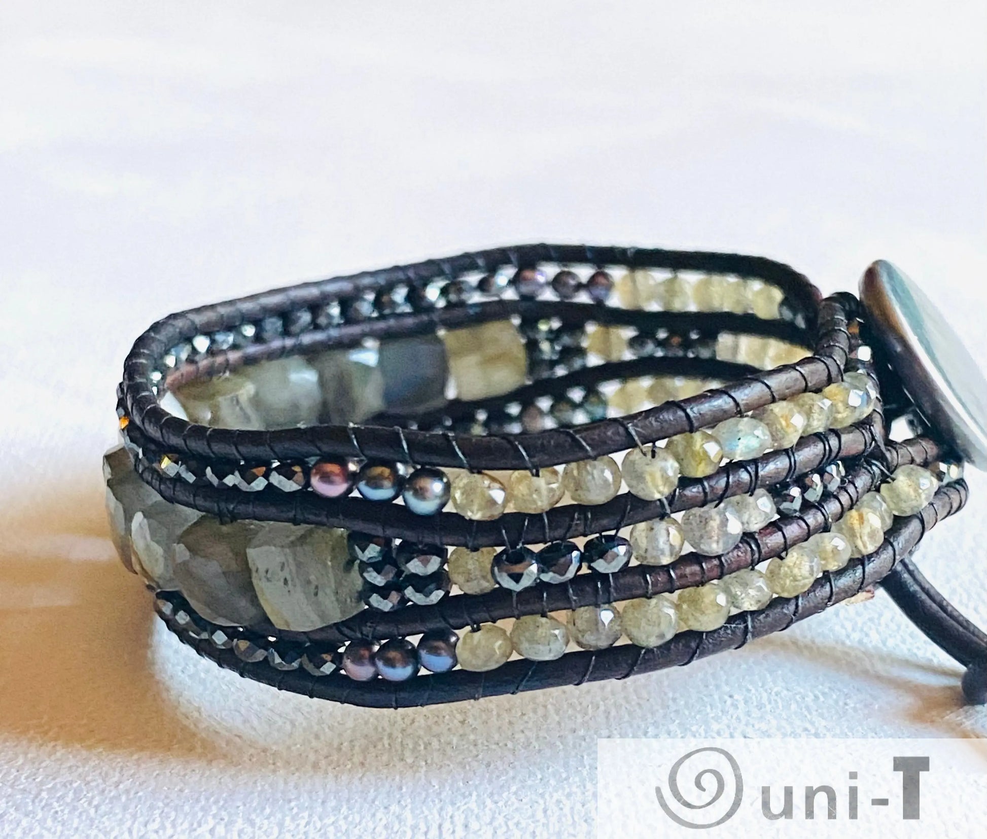 Side view of leather gemstone bracelet with layered strands of labradorite, pearls, and crystals, highlighting intricate beadwork.