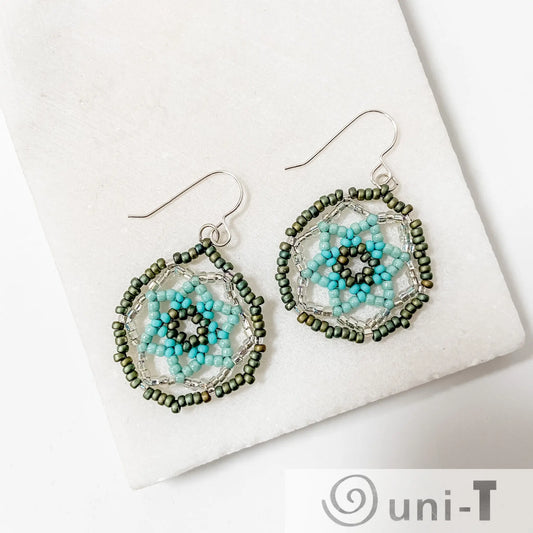 Seafoam green medallion earrings with sterling silver hooks and intricate blue and green floral beadwork, displayed on a white marble background.