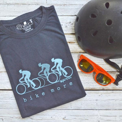 Men's Bicycle T-Shirt in Bamboo & Organic Cotton folded on wood background with helmet and sunglasses, featuring 'Bike More' cycling graphic.