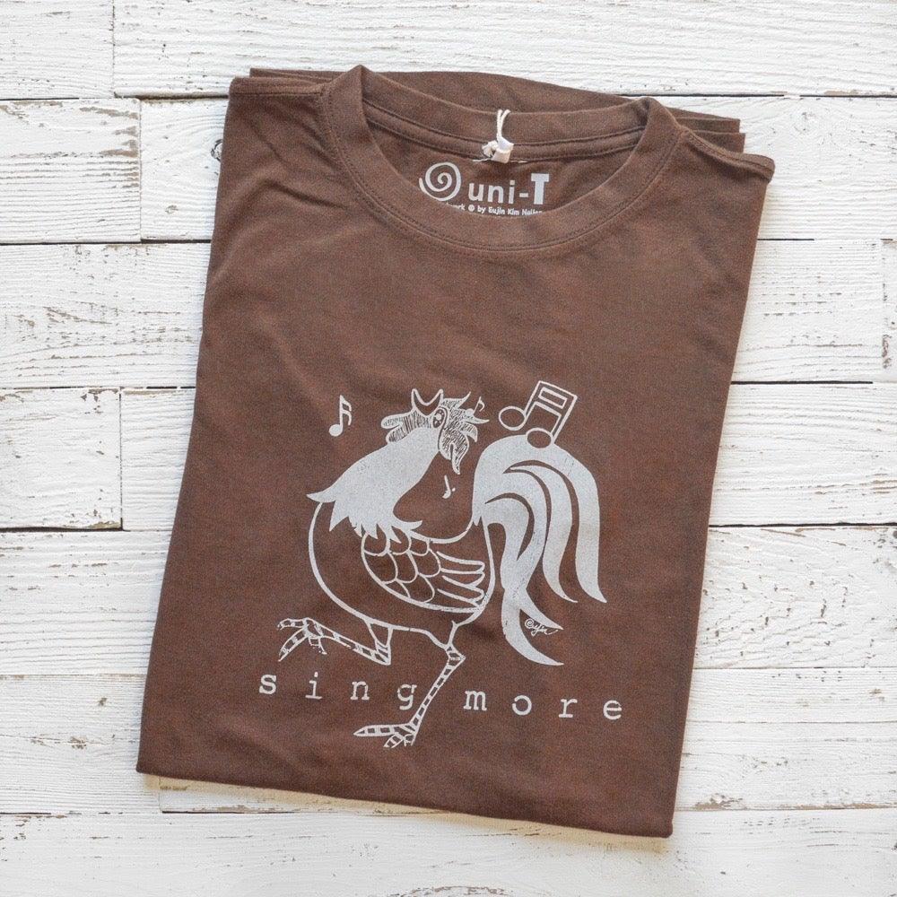 Folded brown 'Sing More' rooster t-shirt for men made from bamboo and organic cotton, featuring a funny farm animal graphic.