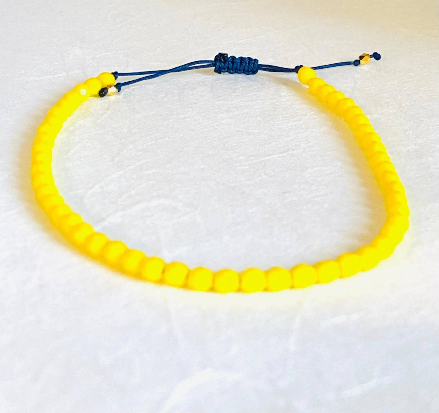 Adjustable friendship bracelet with bright yellow glass beads and blue cord. Stackable design ideal for birthday gifts or casual wear.
