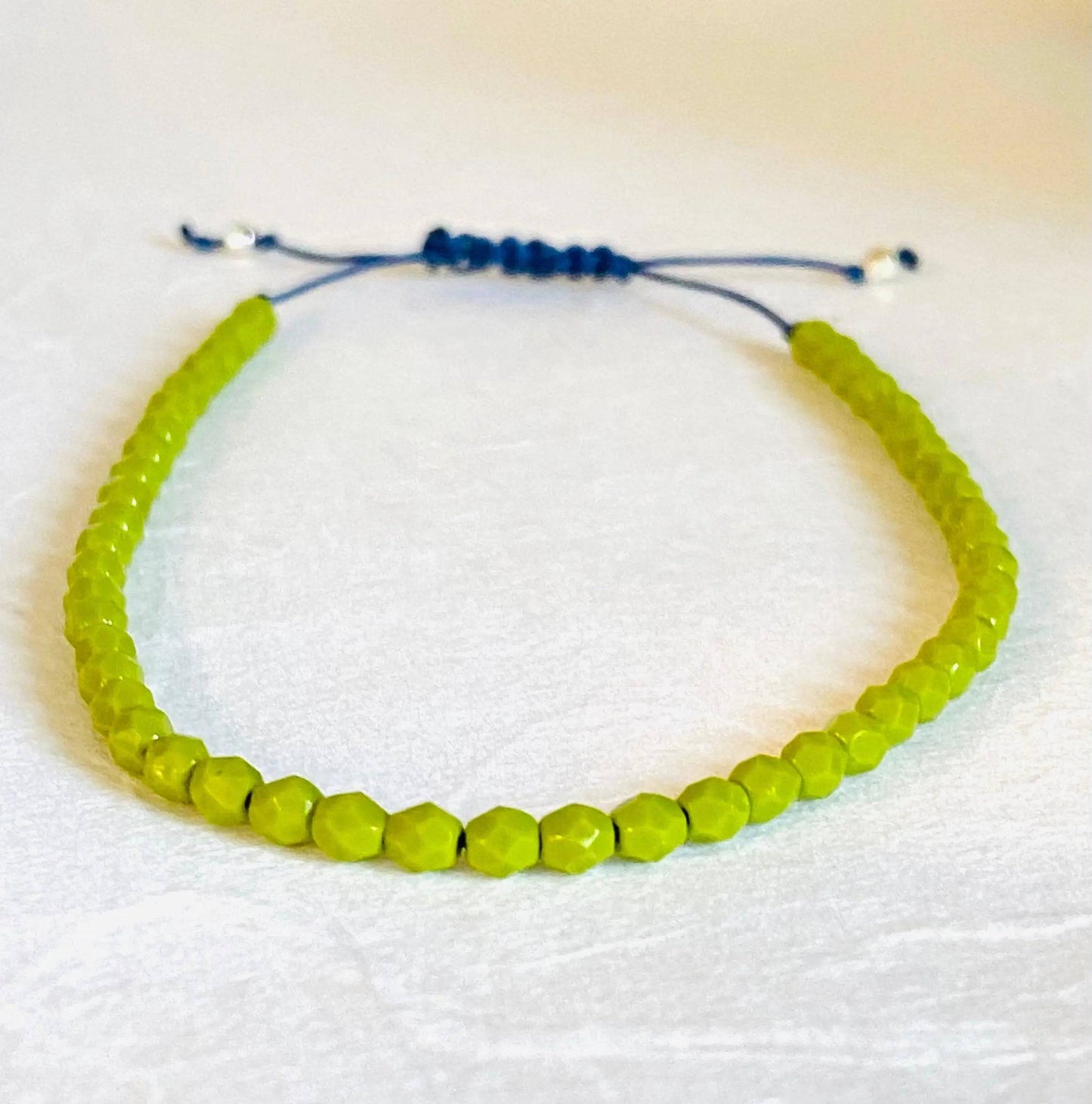 Green glass bead adjustable friendship bracelet with blue cord. Stackable and perfect for gifting or everyday fashion accessories.
