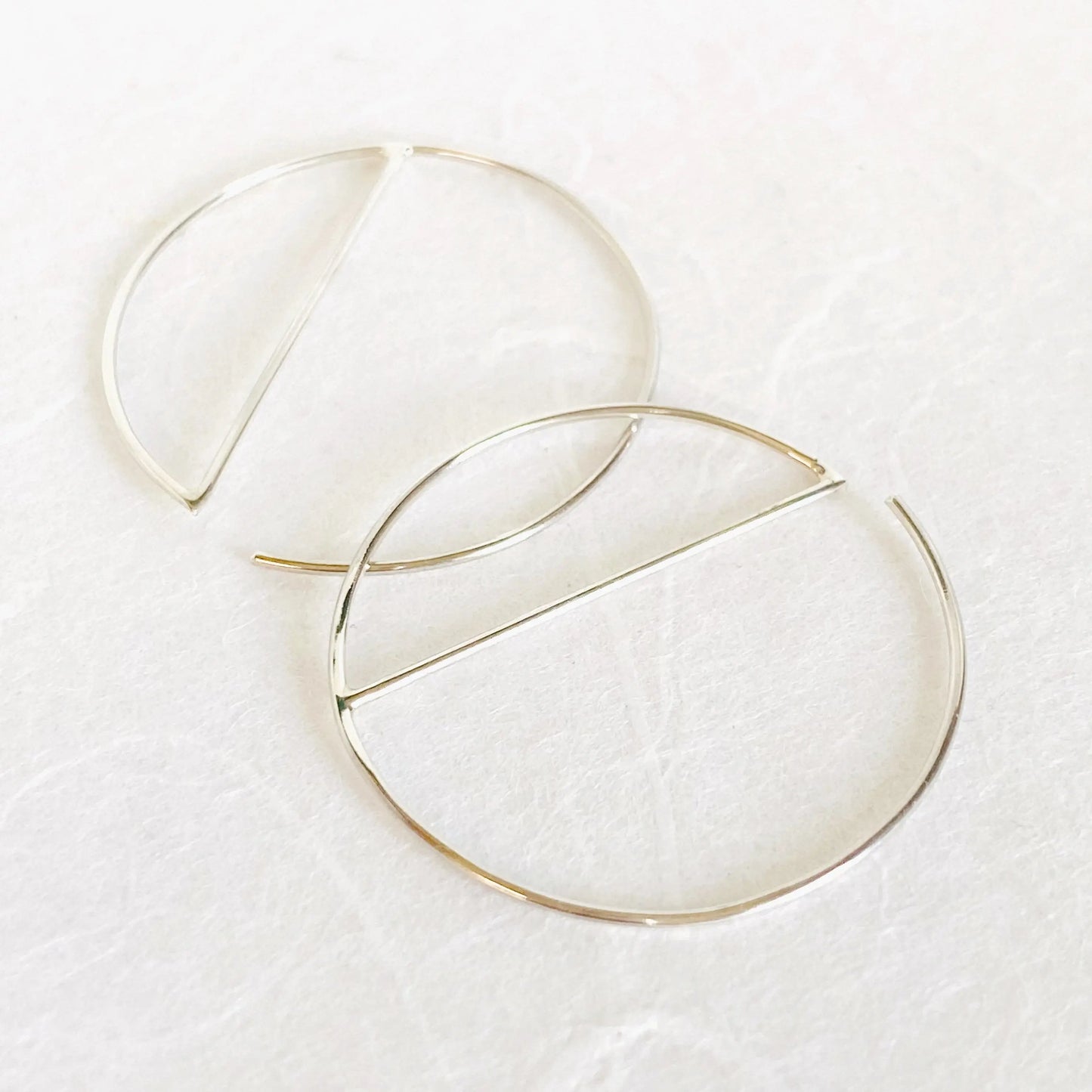 Modern silver hoops in sterling silver with minimalist half-circle bar design. 1” diameter hoop earrings crafted from 21 gauge wire.