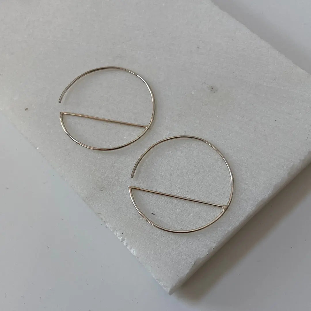 Sterling silver hoop earrings with minimalist bar design, displayed on white stone. 1” diameter modern hoops for versatile styling.