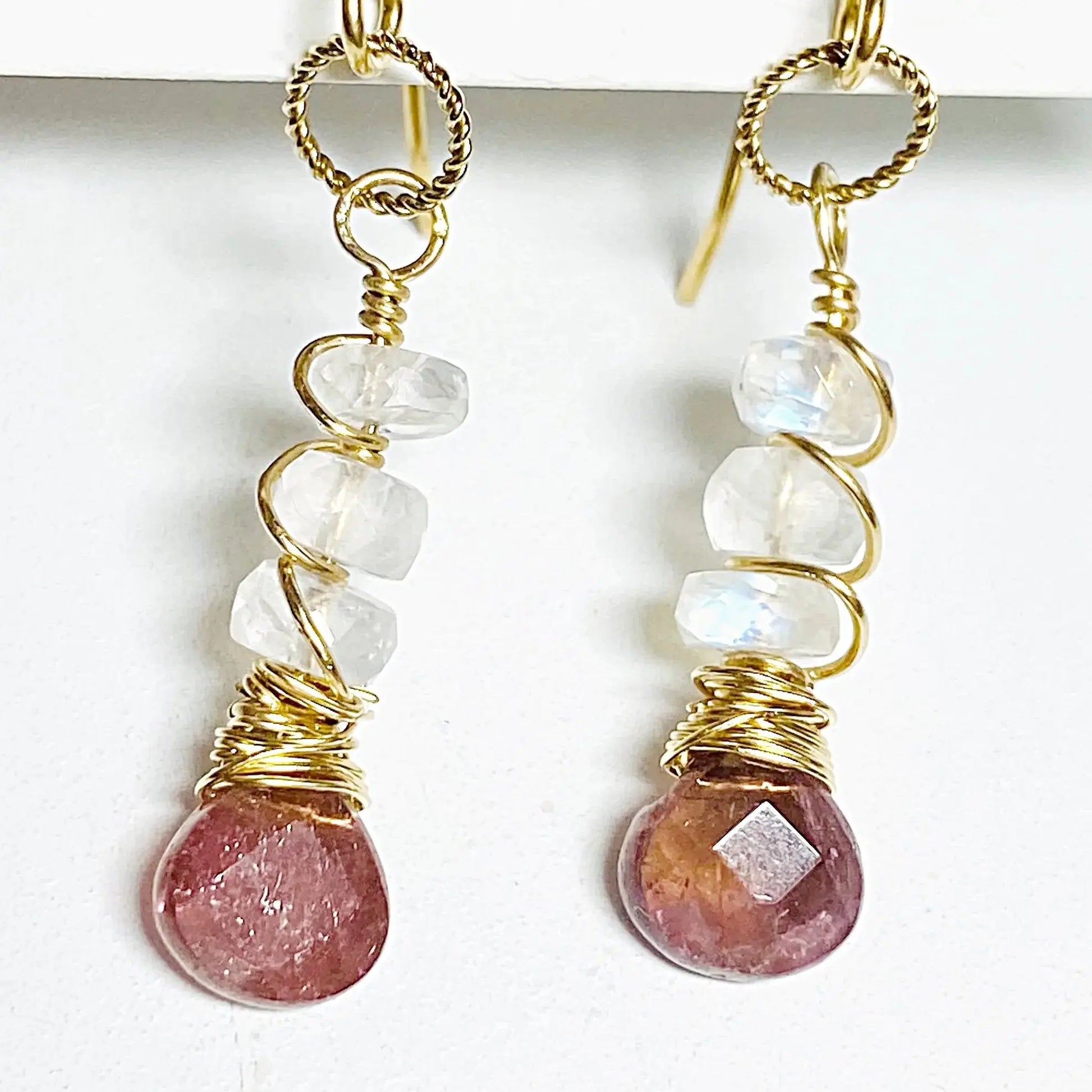 Close-up of moonstone and tourmaline earrings wrapped in gold-filled wire. Handcrafted 1.5-inch gemstone earrings with unique artisan detail.