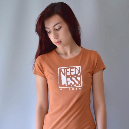 Women's motivational t-shirt in bamboo and organic cotton featuring 'Need Less Do More' quote in rust orange. Minimalist lifestyle tee for her.