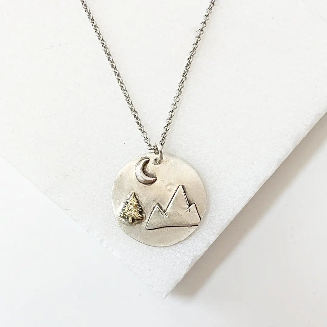 Mountain Medallion Necklace with mountain pendant, brass tree, and crescent moon on 20” antiqued chain. Ideal for outdoor and nature lovers.