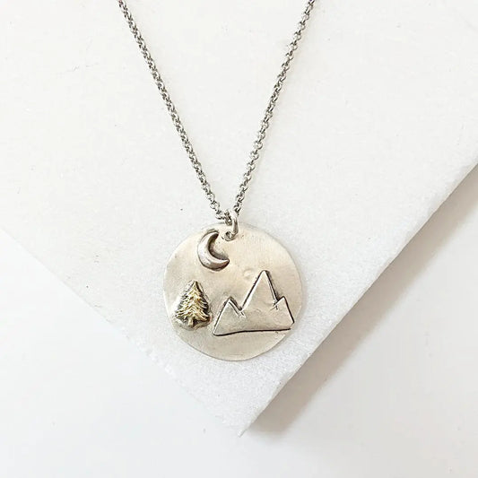 Mountain Medallion Necklace with mountain pendant, brass tree, and crescent moon on 20” antiqued chain. Ideal for outdoor and nature lovers.