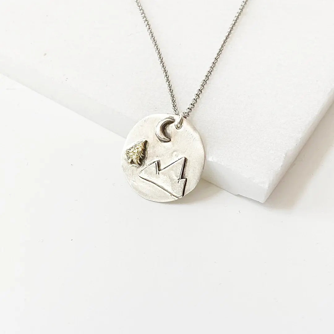 Handcrafted Mountain Pendant Necklace featuring a brass tree and moon on a round medallion with 20” antiqued chain and spring ring clasp.