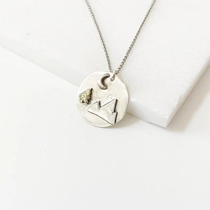 Handcrafted Mountain Pendant Necklace featuring a brass tree and moon on a round medallion with 20” antiqued chain and spring ring clasp.