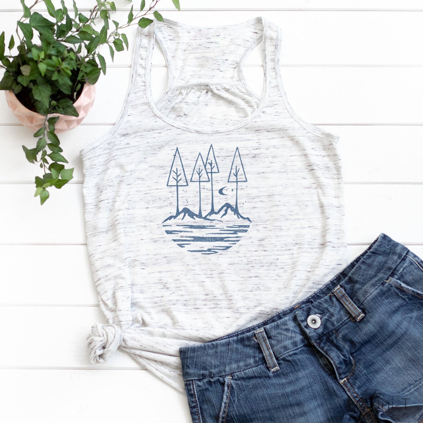 White speckled Nature Flowy Tank Top for Women styled with denim shorts. Features blue mountain and tree design for outdoor lifestyle.