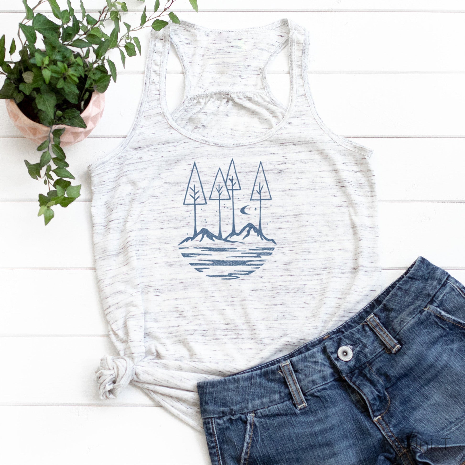 White speckled Nature Flowy Tank Top for Women styled with denim shorts. Features blue mountain and tree design for outdoor lifestyle.