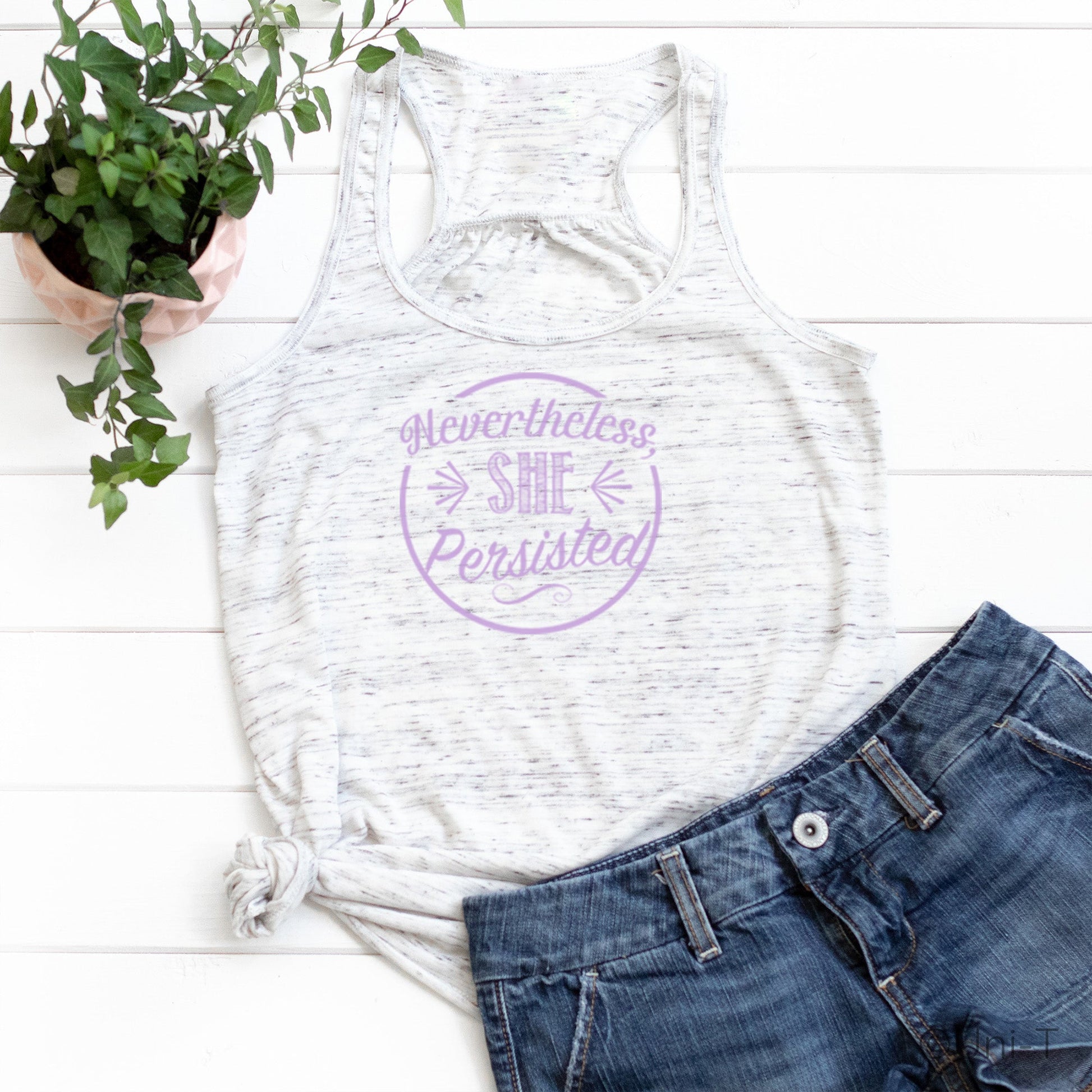 White marbled racerback tank top with purple 'Nevertheless She Persisted' print. Feminist tank styled with denim shorts for casual empowerment.