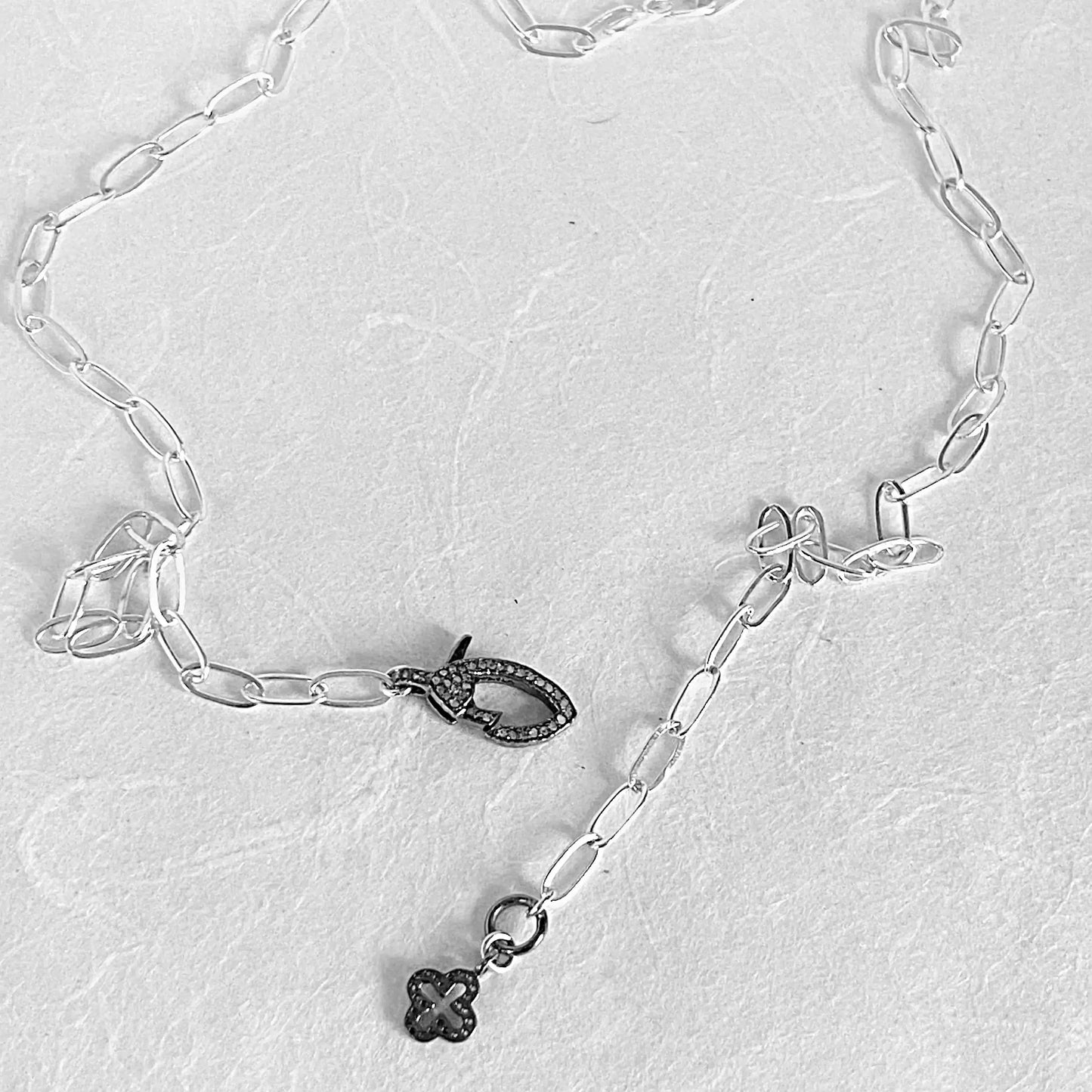 Adjustable sterling silver paperclip chain necklace with moonstone pave clasp and cross-shaped charm, styled for versatile wear.