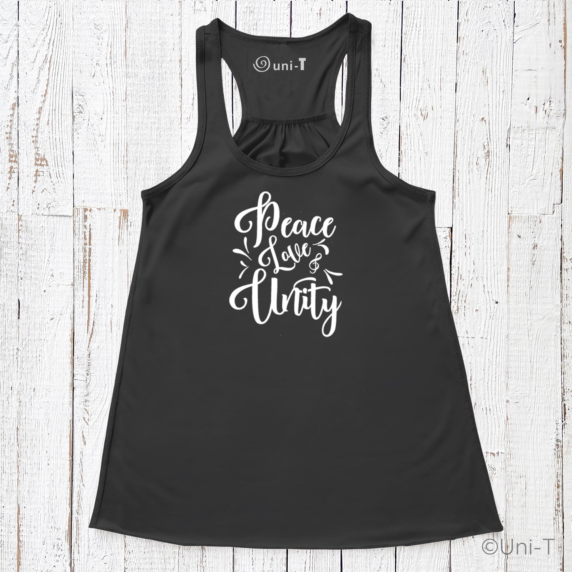 Black "Peace Love Unity" Tank Top - Embrace Harmony with white script text, laid flat on a rustic white wooden surface.
