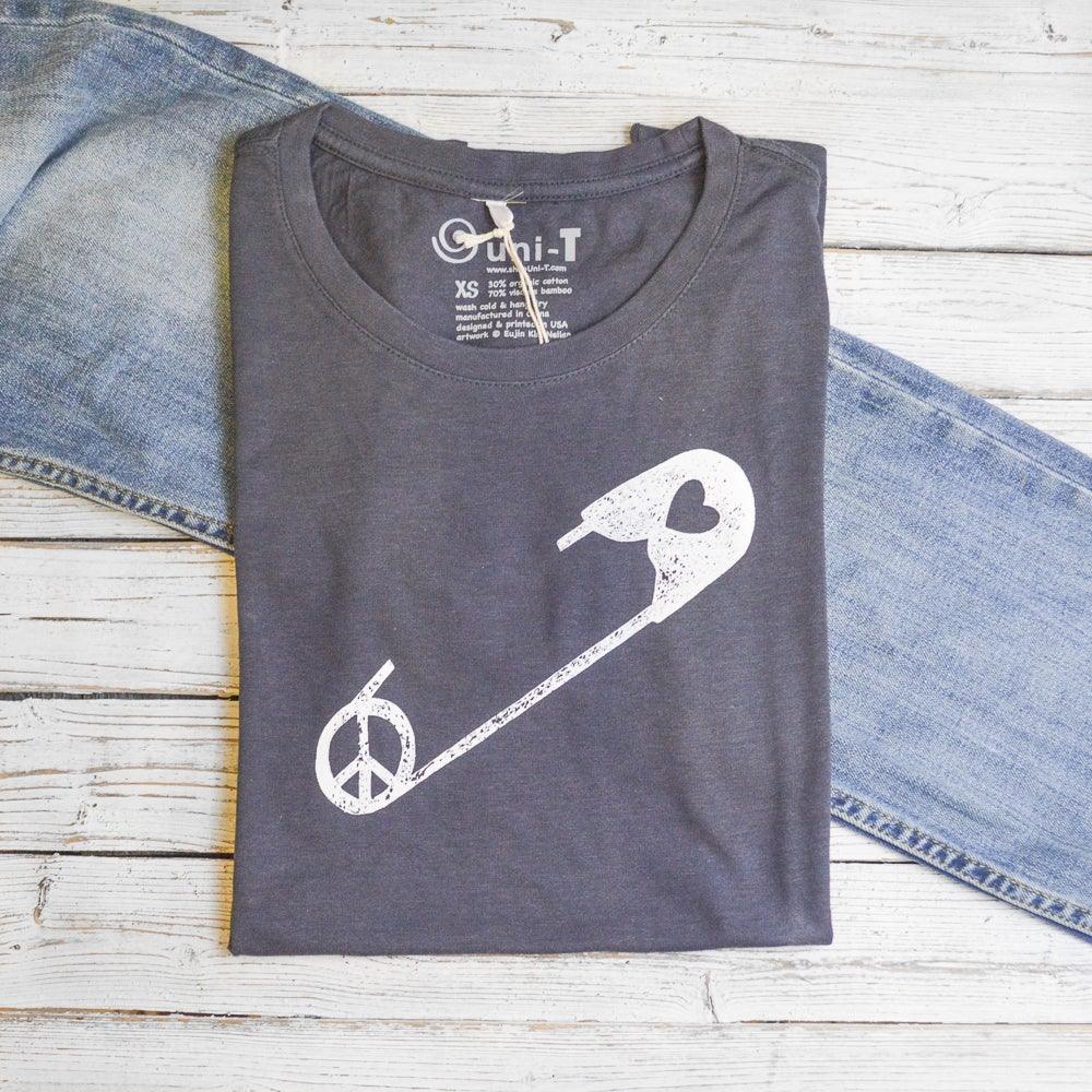 Women's Peace & Love T-Shirt in bamboo and organic cotton, folded in charcoal gray with white safety pin graphic. Eco-friendly activist apparel.