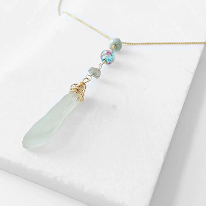 Close-up of Handmade Sea Glass Necklace featuring wire wrapped sea glass pendant, Murano floral bead, and tourmaline accents on a delicate gold chain.