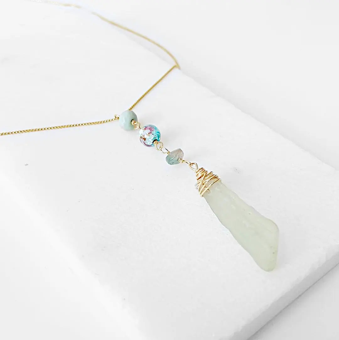 Angled view of Handmade Sea Glass Necklace showcasing wire wrapped sea glass, floral Murano bead, and tourmaline drop on a fine gold necklace.