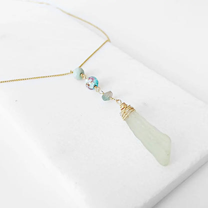 Angled view of Handmade Sea Glass Necklace showcasing wire wrapped sea glass, floral Murano bead, and tourmaline drop on a fine gold necklace.
