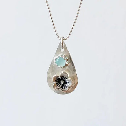 Silver flower necklace with chalcedony teardrop pendant on a 1 mm beaded chain. Features a sterling silver floral design and soft blue gemstone.