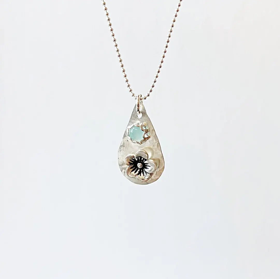 Silver flower necklace with light blue chalcedony gemstone on a ball chain. Teardrop pendant crafted in sterling silver with floral accent.