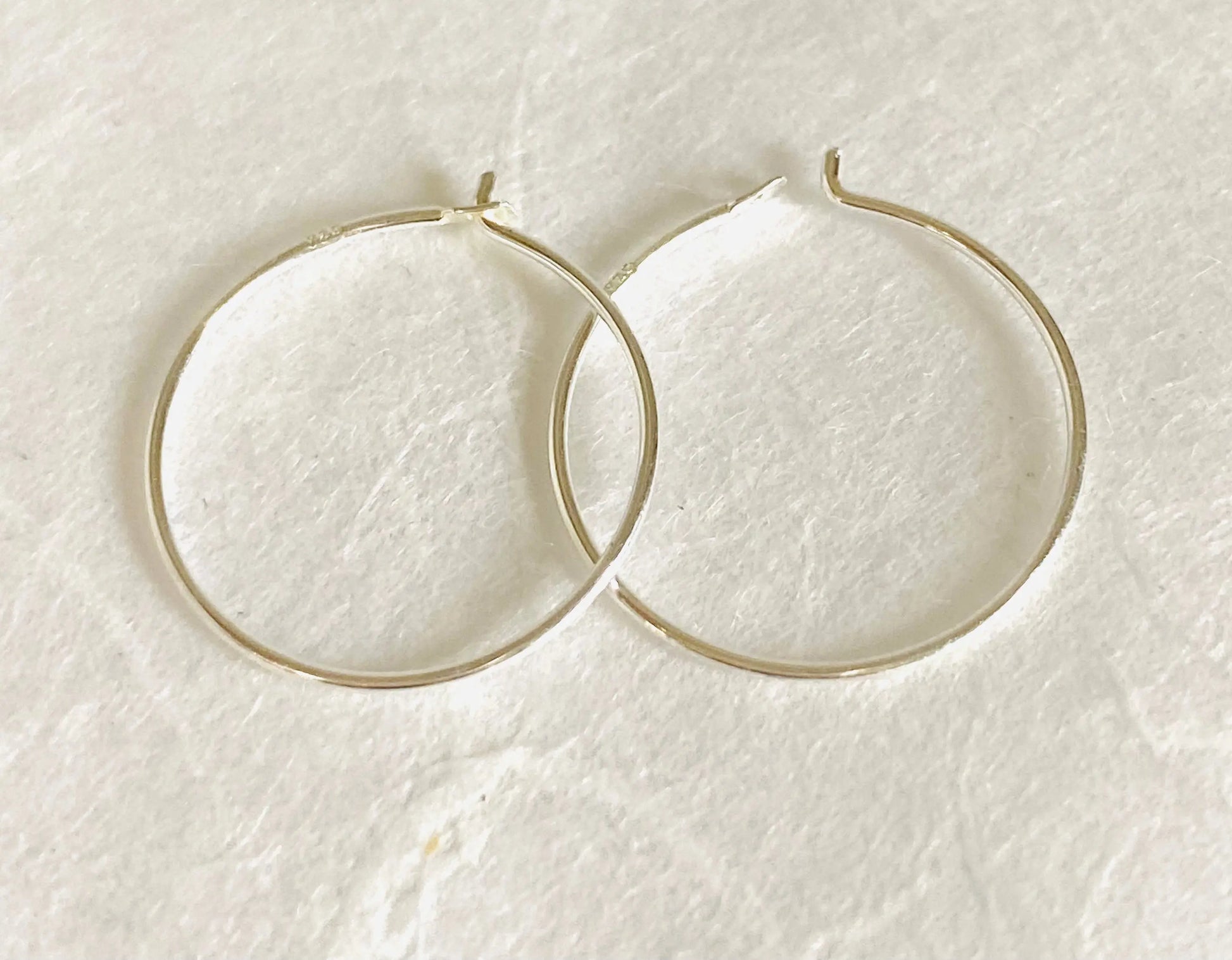 Pair of simple sterling silver hoops, 3/4” diameter, displayed flat on white background. Classic minimalist earrings in fine 22 gauge silver.