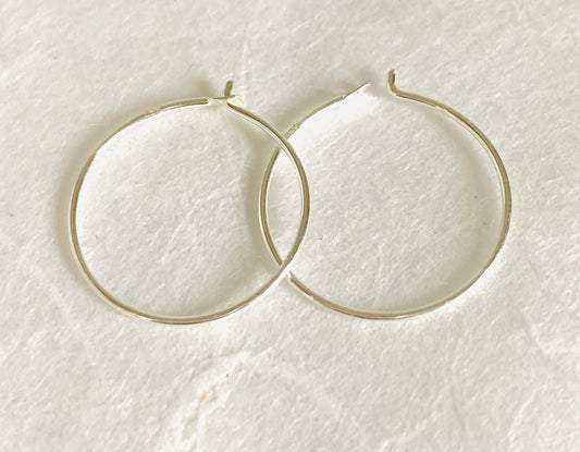 Pair of simple sterling silver hoops, 3/4” diameter, displayed flat on white background. Classic minimalist earrings in fine 22 gauge silver.