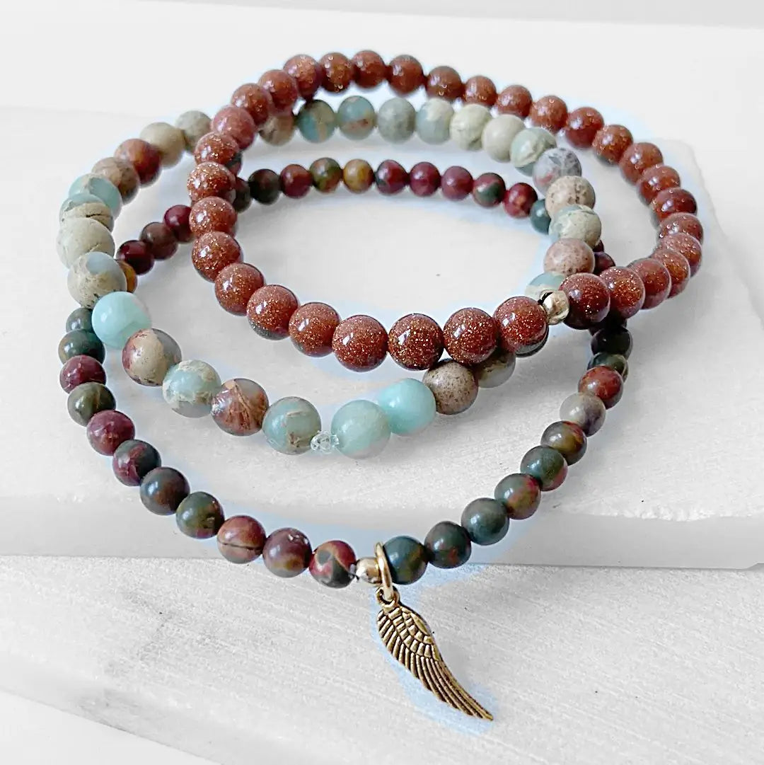 Triple Bracelet Stack featuring Ocean Jasper, Goldstone, and forest jasper beads in earthy tones, includes a brass wing charm centerpiece.