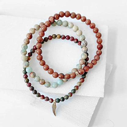 Stylish Triple Bracelet Stack with shimmering Goldstone, Ocean Jasper, and forest jasper beads, highlighted by a brass wing charm.