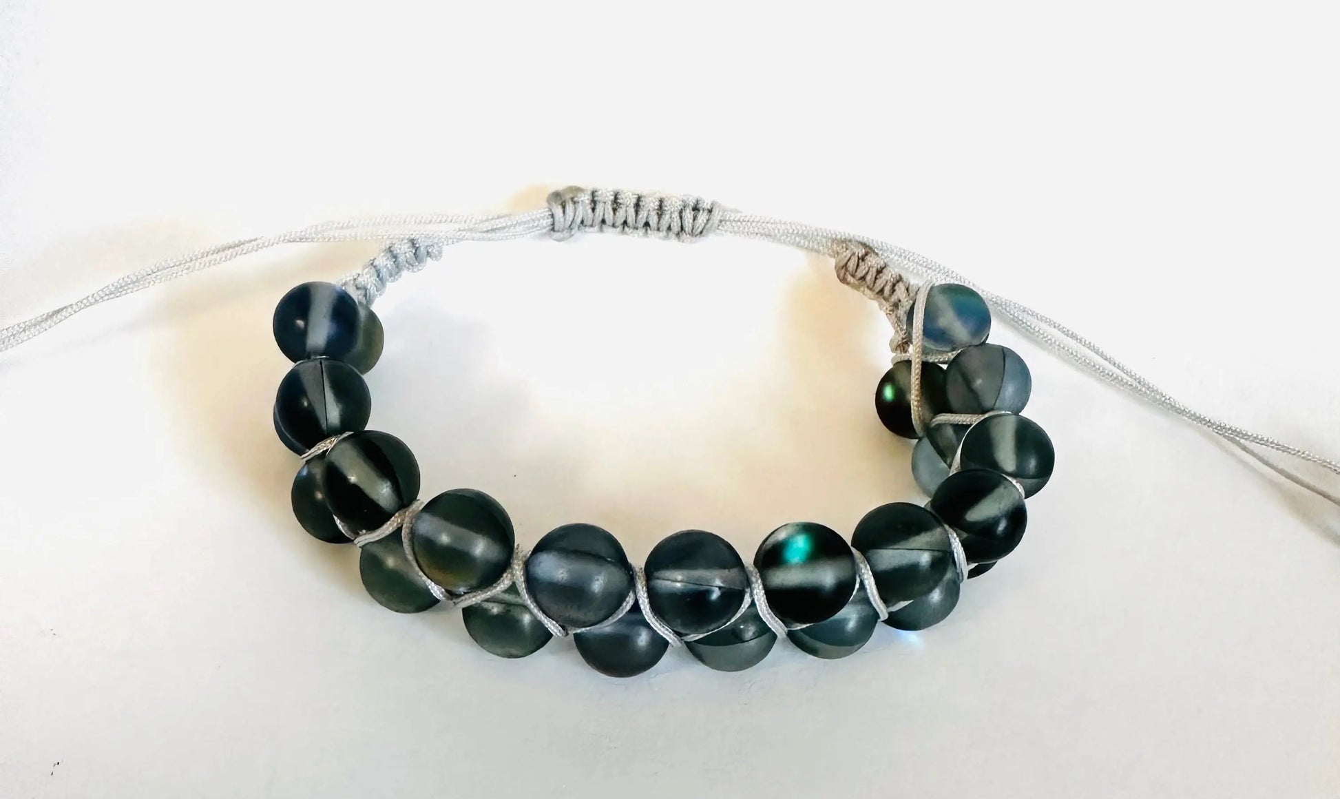 Dark green gemstone bead bracelet with white nylon cord in adjustable woven design. Stylish accessory for men and women.