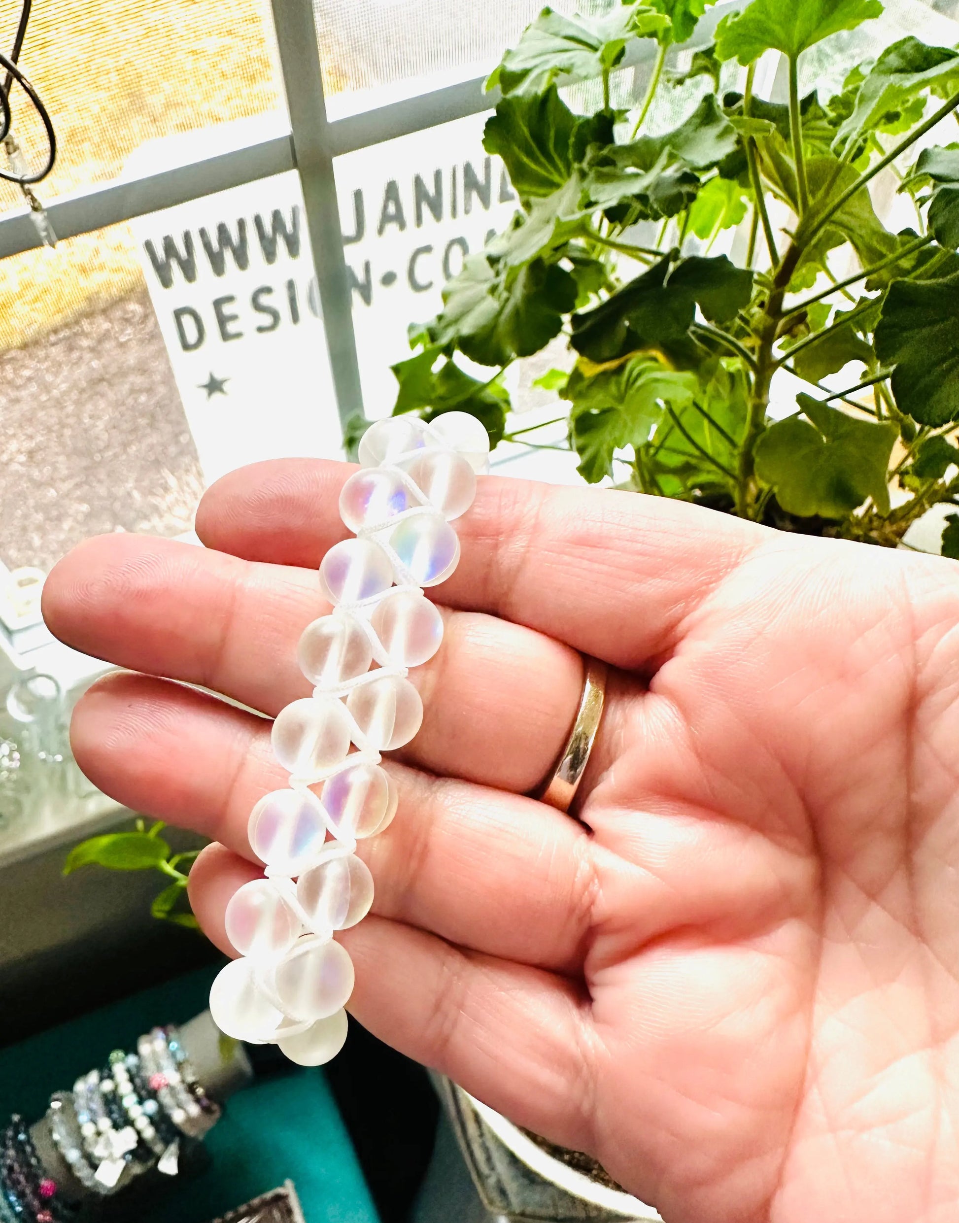 Hand holding a frosted white glass bead bracelet near a window. Showcases the adjustable woven nylon bracelet in natural light.